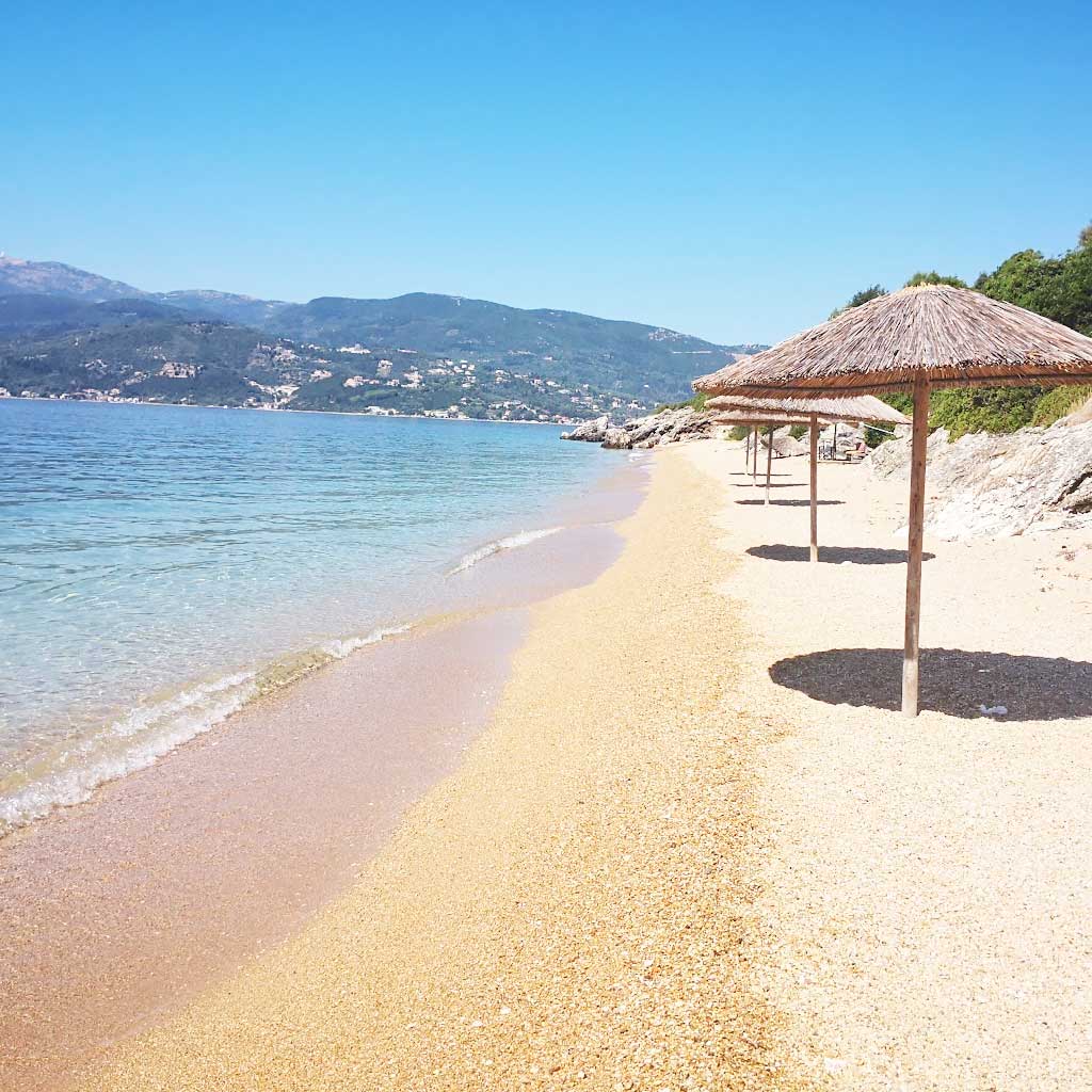 Sandy beach and straw umbrellas in Lygia, Lefkada, showcasing the area's real estate appeal.