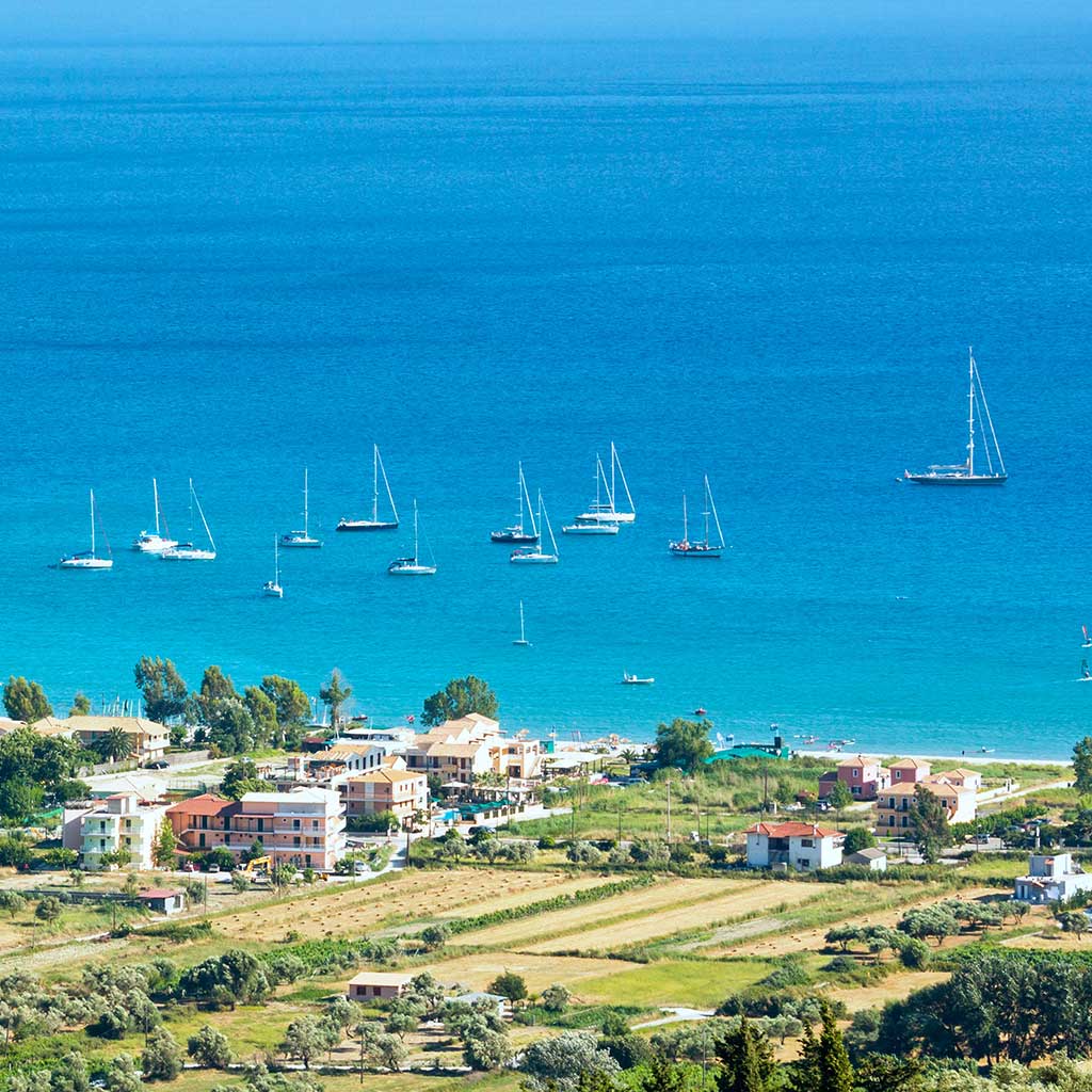 Sailboats moored off the coast near Vasiliki, Lefkada, with coastal homes in view.