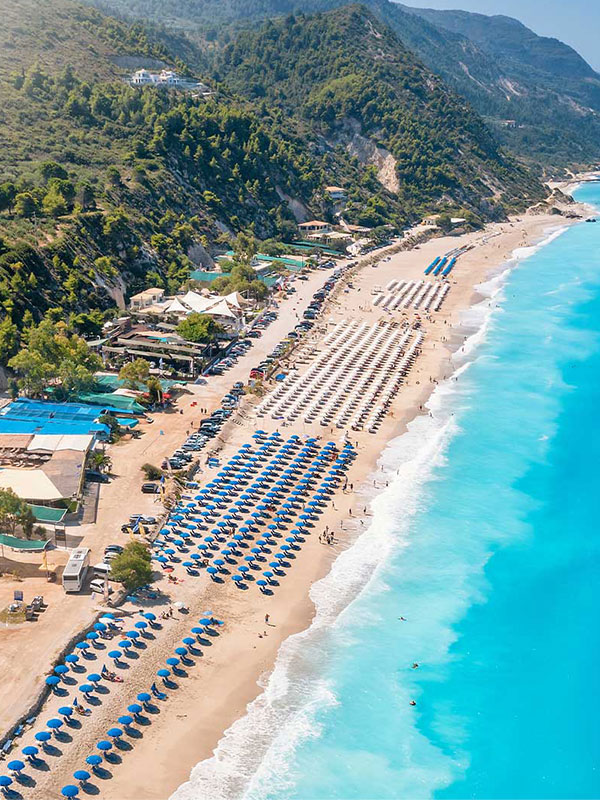 Aerial view of a bustling beach in Lefkas, showcasing potential real estate investment opportunities along the coastline.