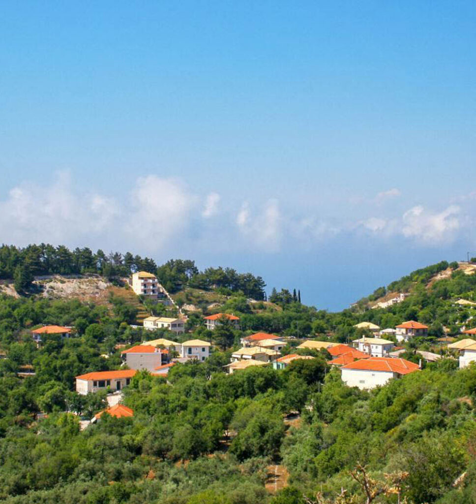 Hillside view of residential properties in Kalamitsi, Lefkada, featuring terracotta-roofed houses amid lush greenery, highlighting the serene and inviting real estate opportunities in the area.