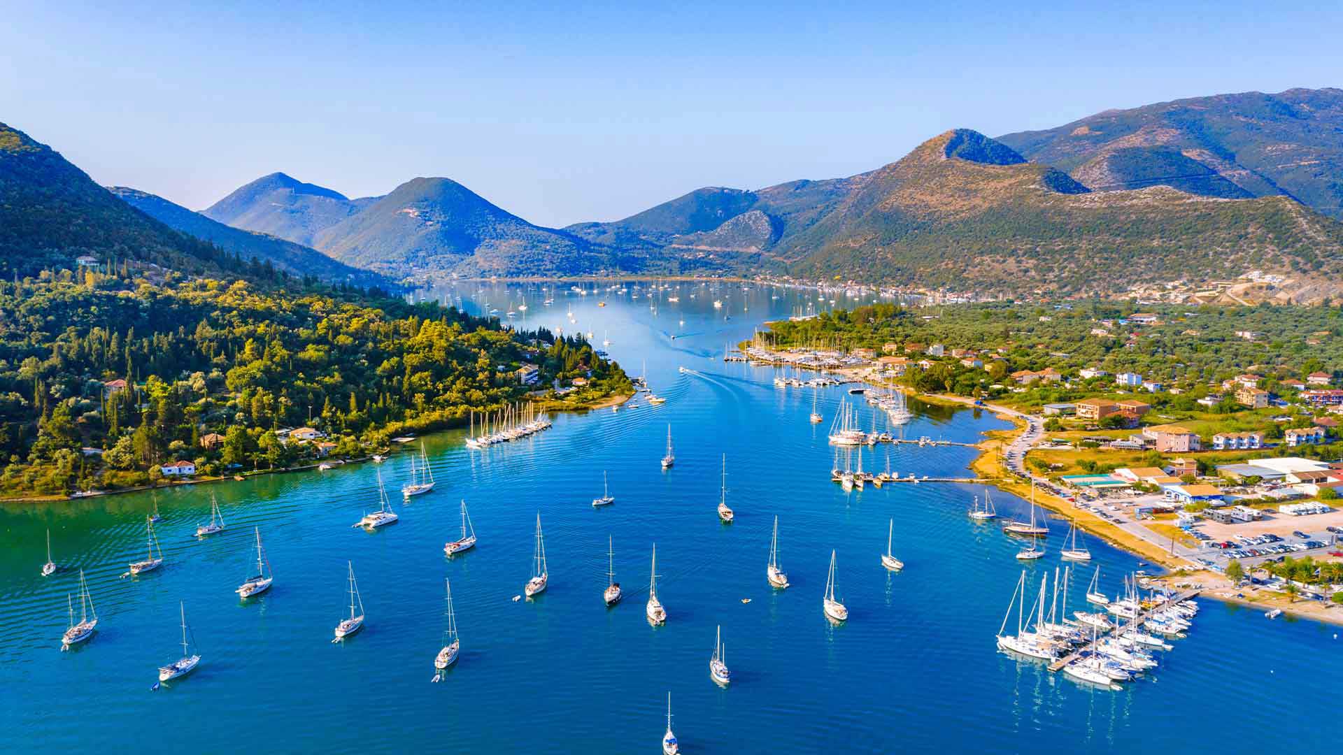 Aerial view of Nydri's vibrant marina in Lefkada, surrounded by lush hills, prime for real estate.