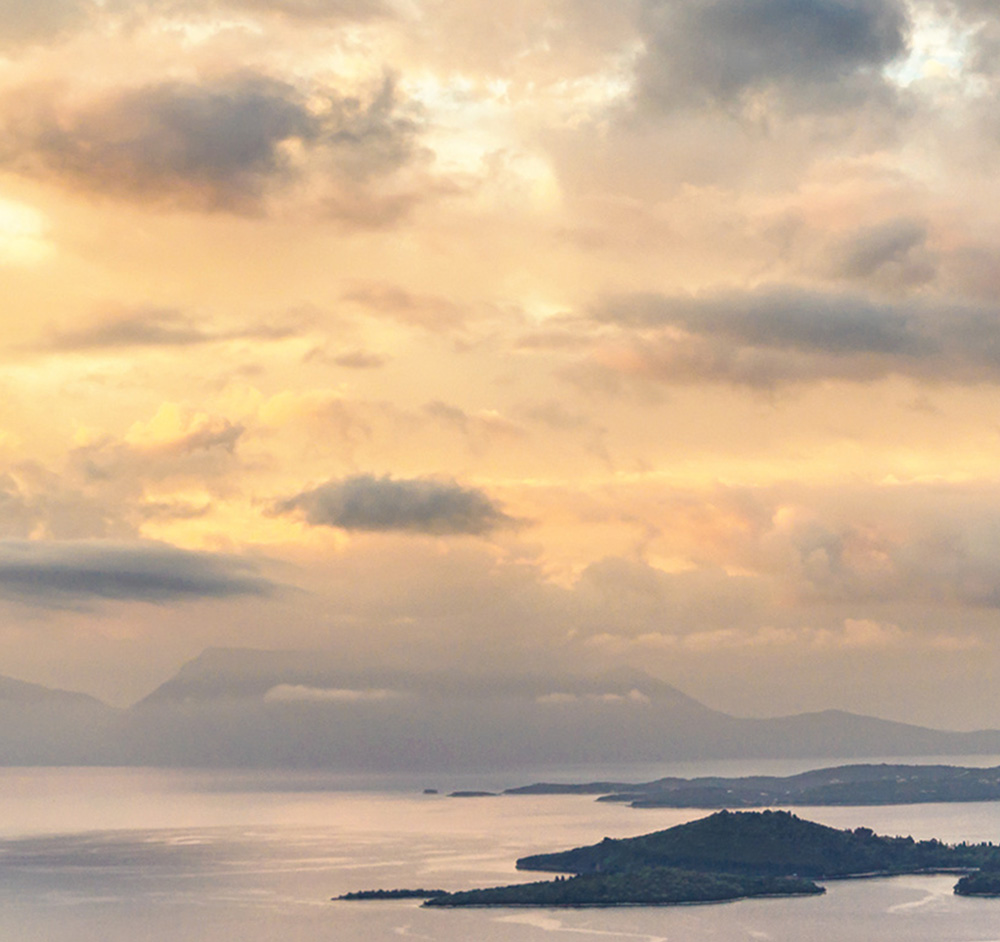 Dusk settles over the serene Perigiali shoreline with Lefkada's real estate silhouetted against the sky.